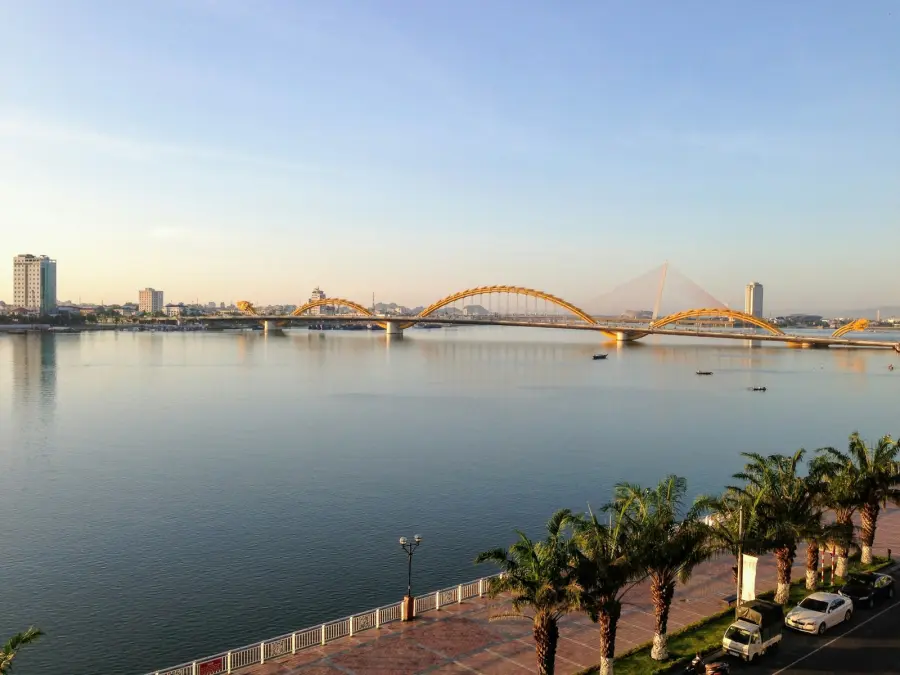 Low sun on the Han River: the Dragon Bridge and its golden arches across still water, palms along the riverside promenade