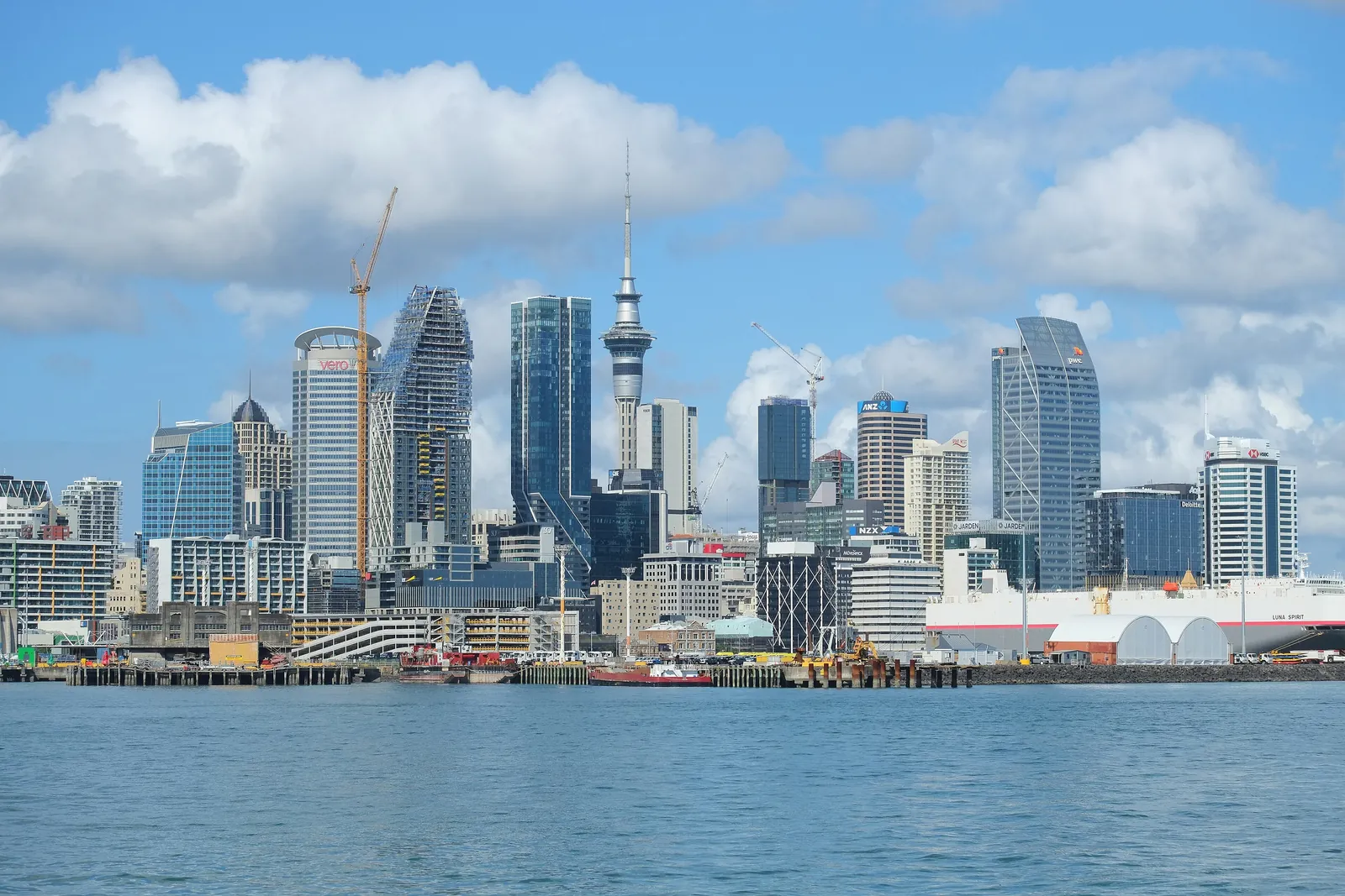 Auckland's city centre and the Sky Tower seen across the Waitematā Harbour from the water, under a big summer sky