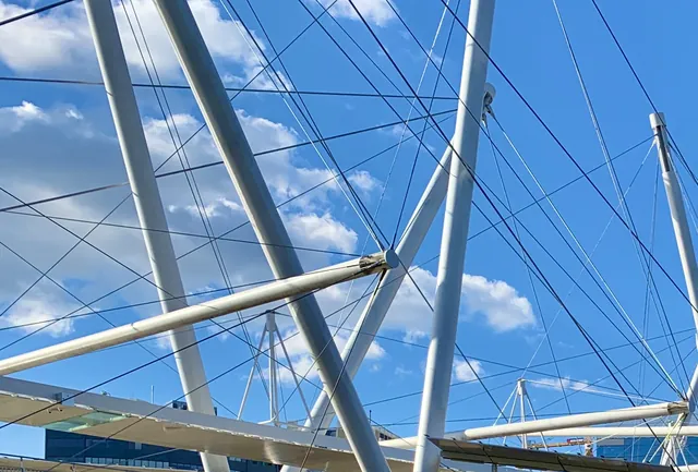 Kurilpa Bridge's slim white masts leaning at different angles, with fans of cables and floating spars against a blue sky