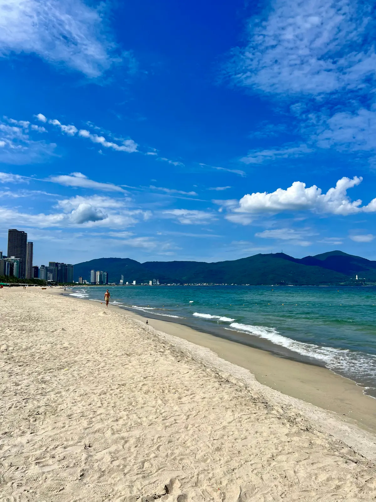 My Khe beach under a hot blue sky, pale sand curving toward the city and the Son Tra mountains