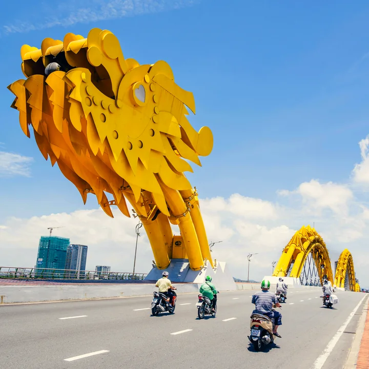 The finished puzzle: the golden Dragon Bridge head over a Da Nang road at midday, motorbikes crossing