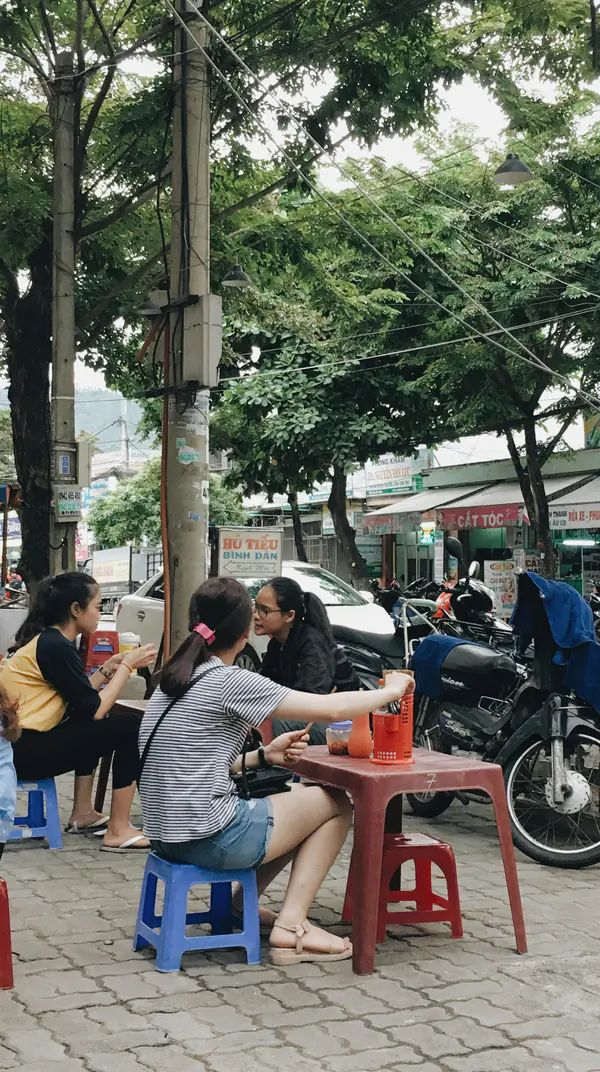 Friends on low plastic stools at a Da Nang pavement cafe, drinks on a red table