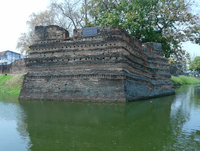 A weathered red-brick corner bastion rising in layered courses straight out of the green moat, a stone plaque set on its top