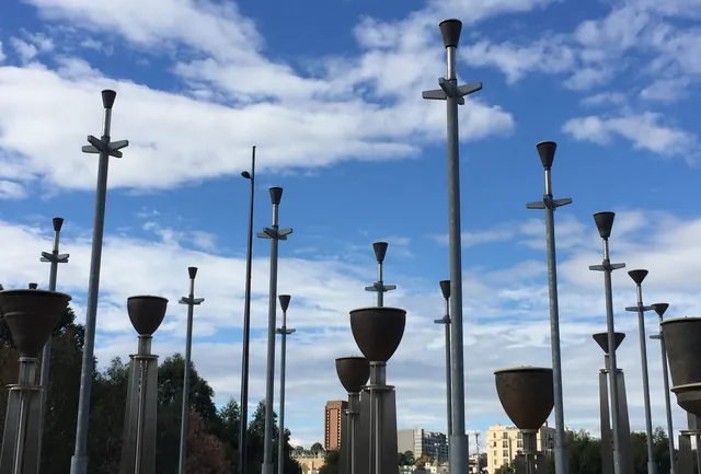 The Federation Bells in Birrarung Marr: upturned bronze bells on tall steel poles against a blue sky with white cloud