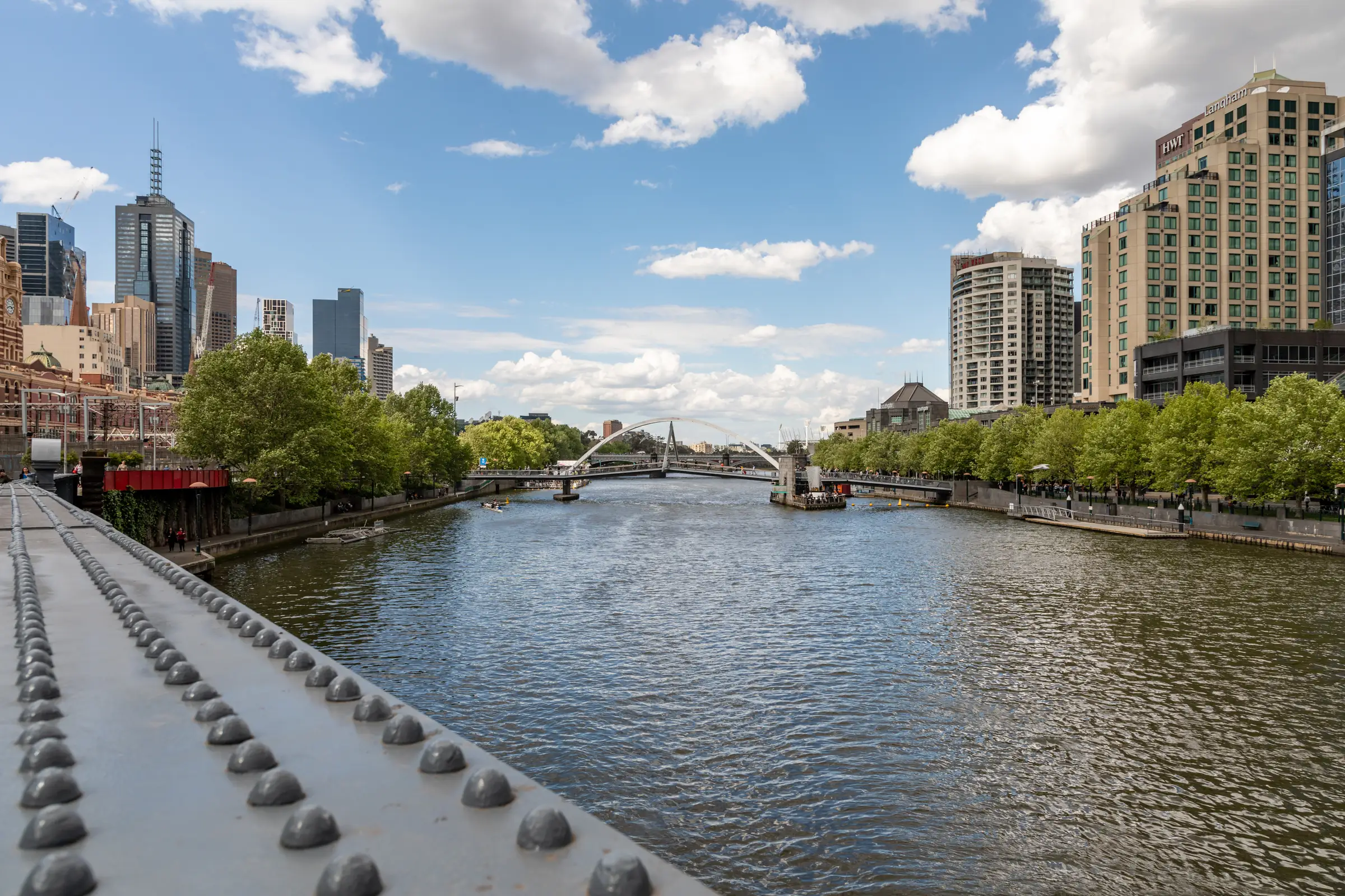 The Yarra from Princes Bridge on a bright day with big white clouds: the river running west between tree-lined banks, the city towers on the right and Southbank on the left