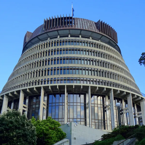 The Beehive, the round, stepped executive wing of Parliament, its copper crown and flag against a clear blue sky above the trees