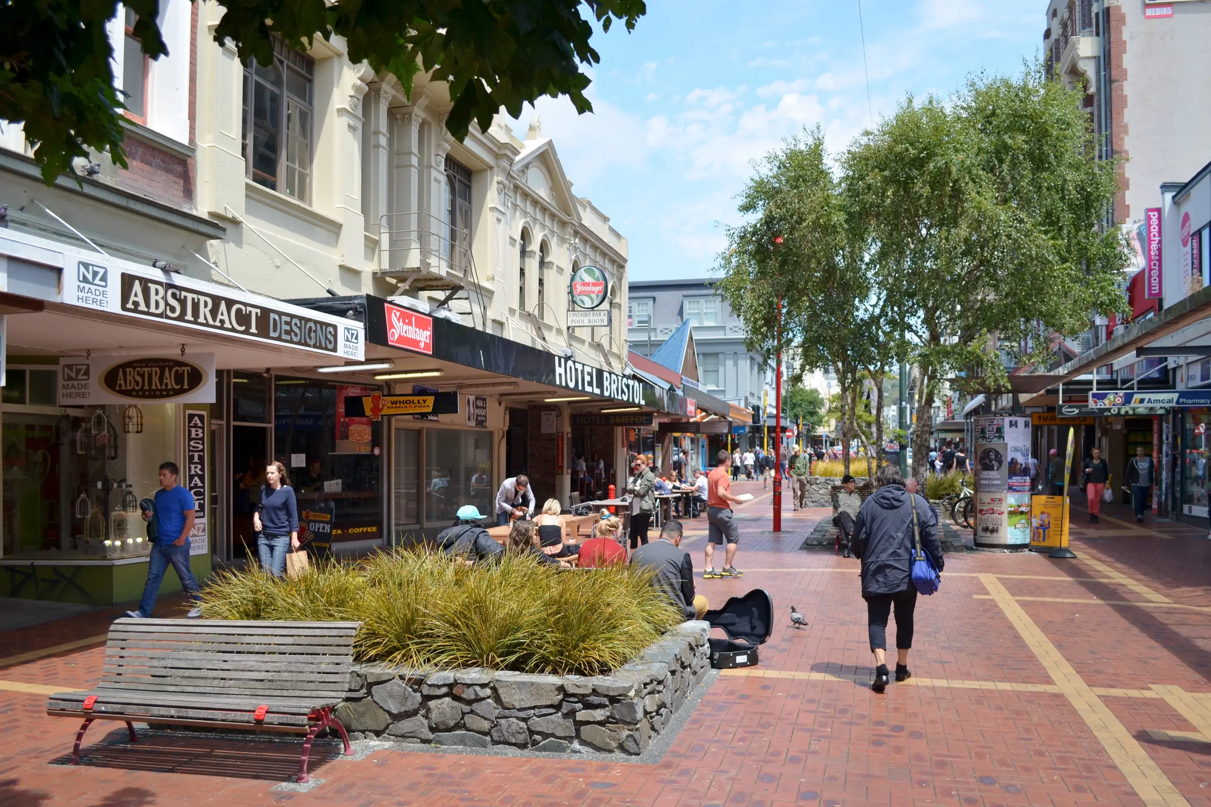 Cuba Mall on a sunny day: people walking and sitting out on the red brick paving under birch trees, old shopfronts and verandas on both sides